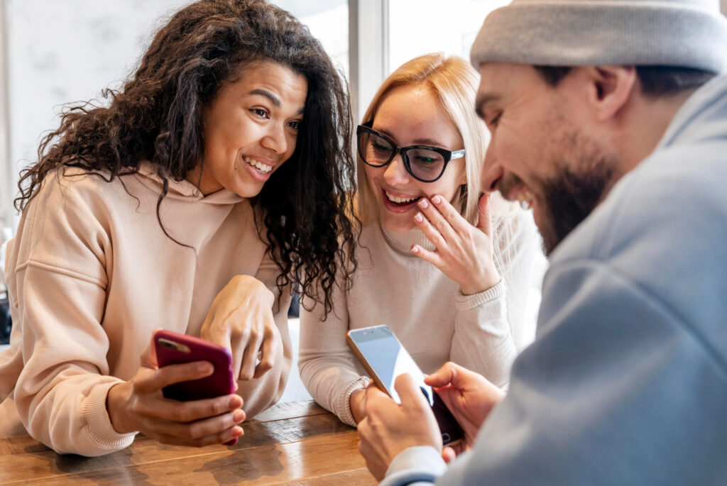 Three friends smiling while looking at smartphones together
