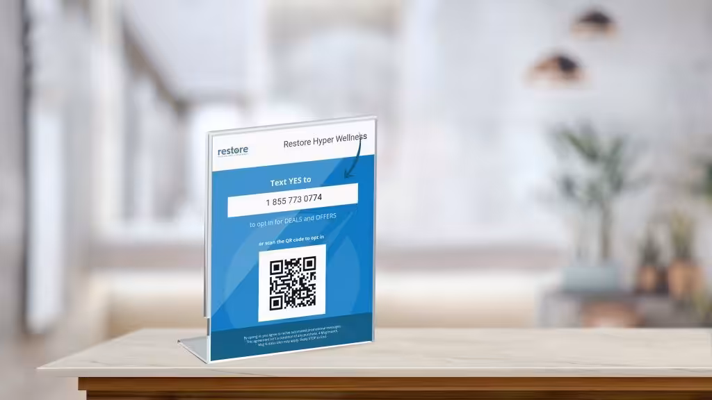 A sign for Restore Hyper Wellness encourages customers to text "YES" to a number or scan a QR code to opt-in for deals.