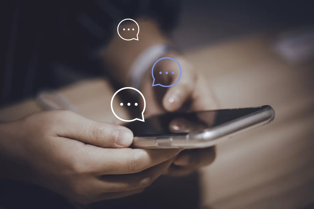 Hands holding a smartphone. 3 icons of chat clouds indicate the person holding the phone is texting someone.